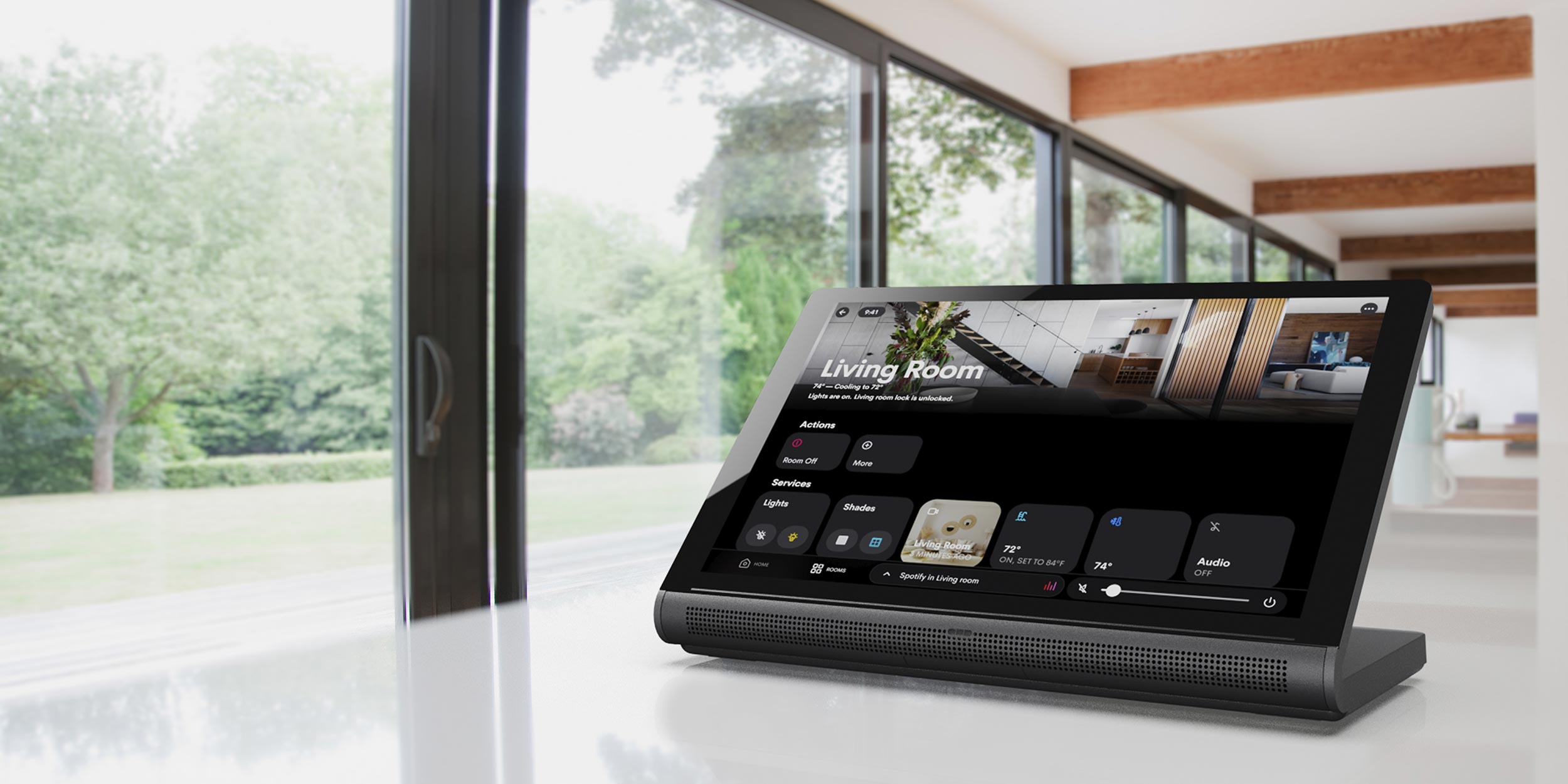 A smart home control device on a countertop with a view of a bright living space and green outdoor scenery.